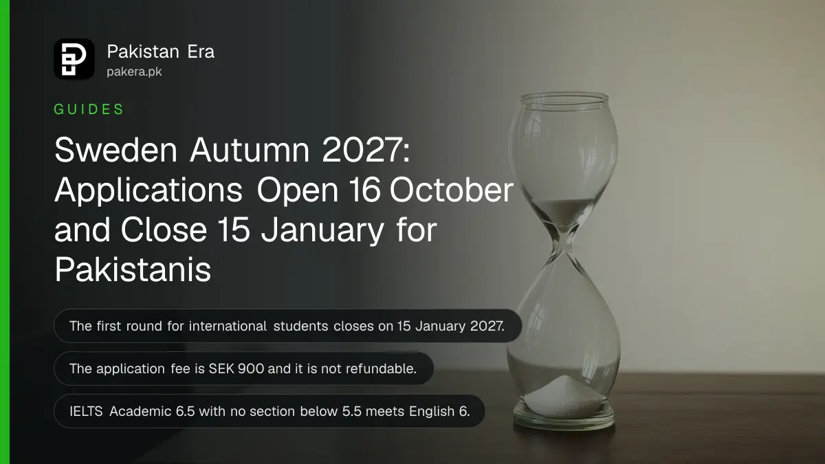 A glass hourglass with sand on a dark wooden table against a plain cream wall in soft daylight