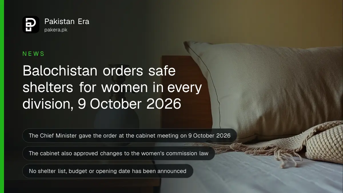 A folded blanket, a pillow and a small lamp on a plain wooden bed in a bare room with a cream wall