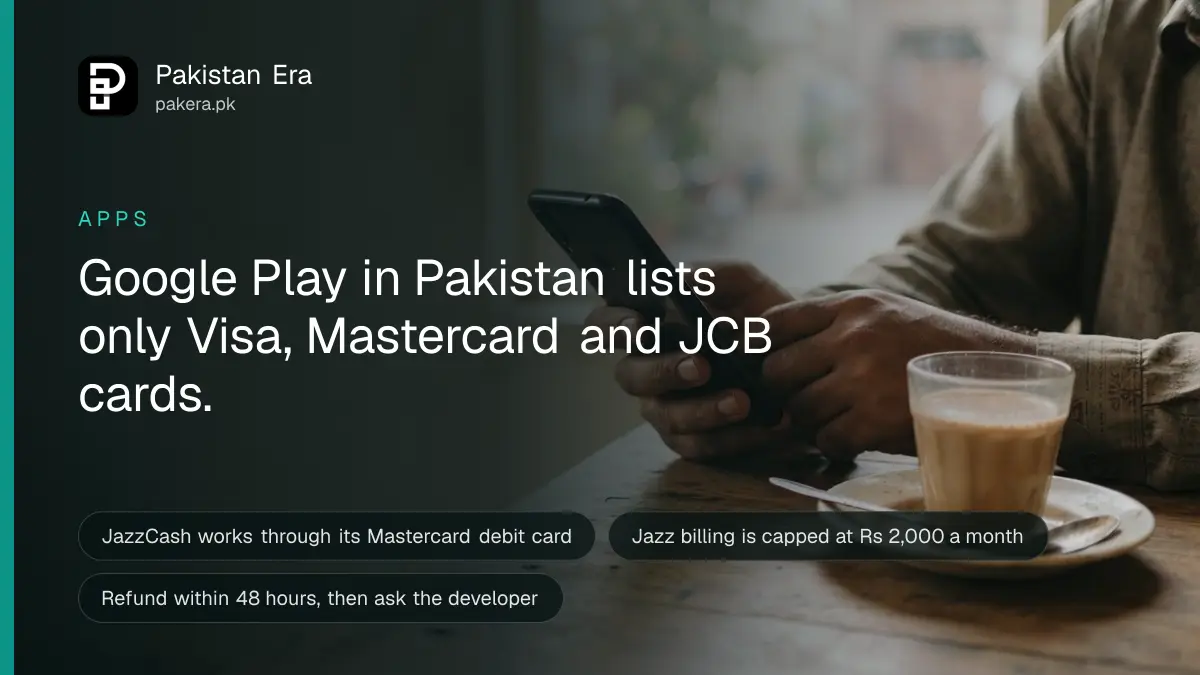 Hands holding a phone with a dark screen above a wooden table beside a cup of chai in Lahore