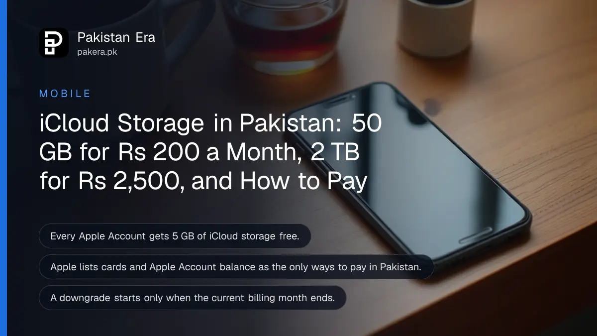 A smartphone lying face up with a dark screen on a wooden desk beside a cup of tea and a small potted plant