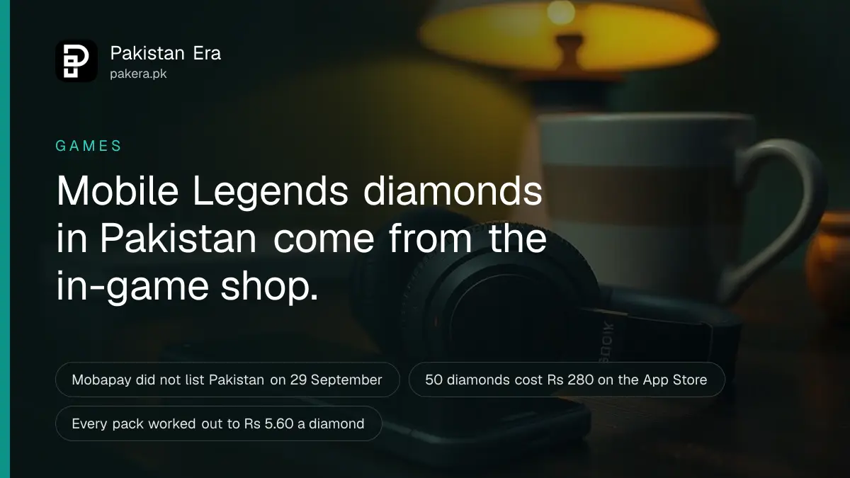 A pair of black wireless headphones on a wooden desk beside a smartphone lying face down under a warm lamp in Peshawar
