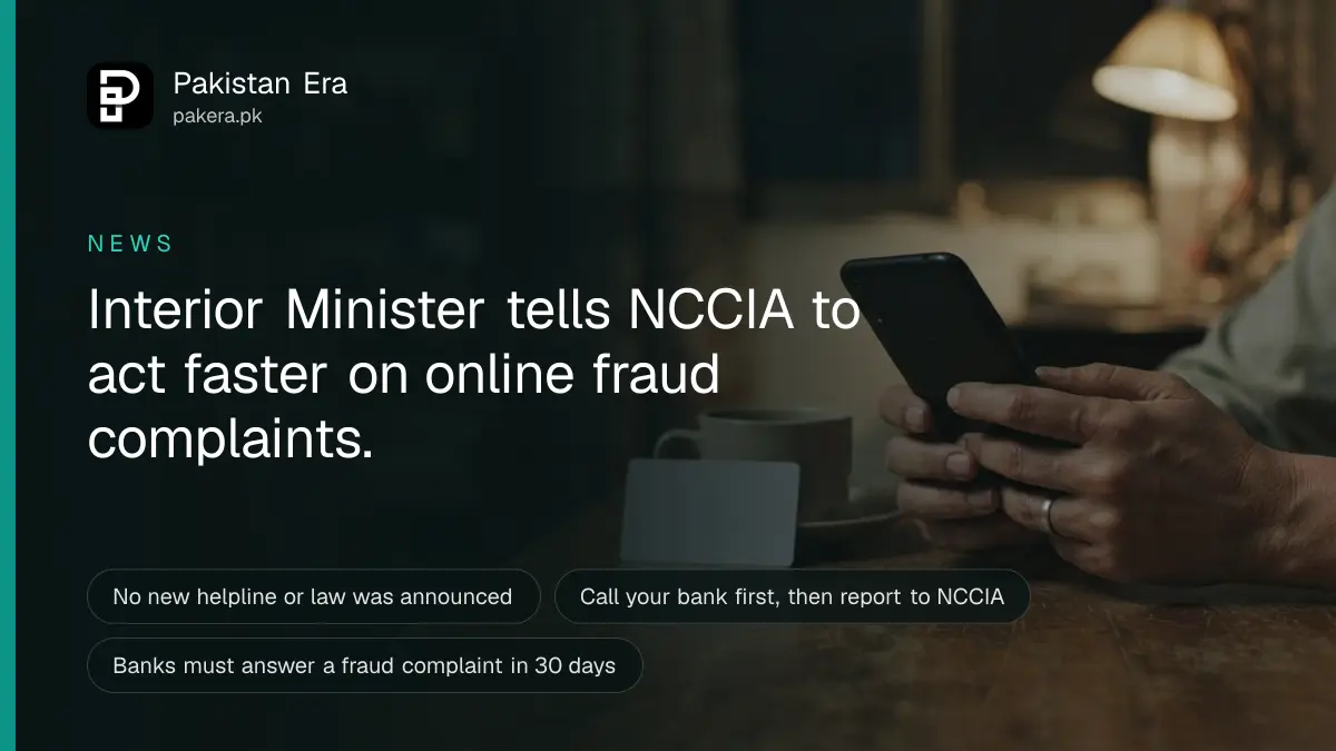 Hands holding a smartphone face down beside a bank card and a cup of tea on a wooden table at night