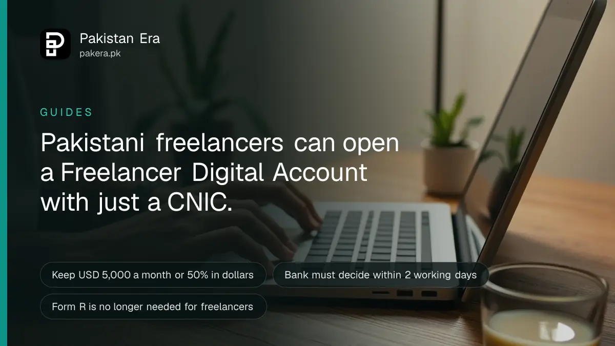 A freelancer's hands typing on a laptop keyboard beside a smartphone and a cup of tea at home