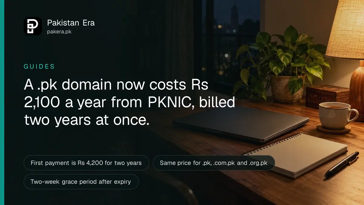 A closed laptop beside a notebook and a cup of tea on a wooden desk at night