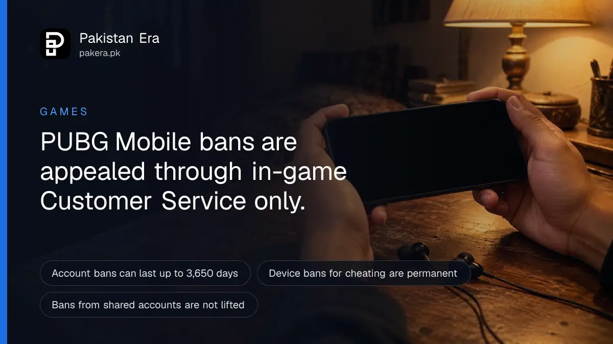 Two hands holding a phone sideways with a dark screen, lit by a desk lamp at night